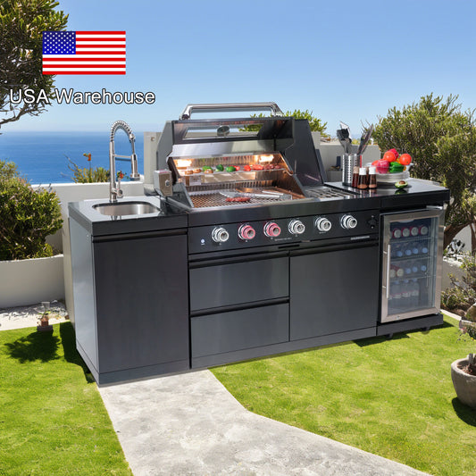 Outdoor kitchen with grill, sink, and refrigerator on a grassy area with ocean view.